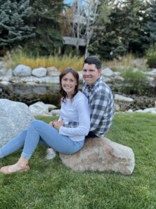 Adrienne sits in front of Stuart on a boulder.